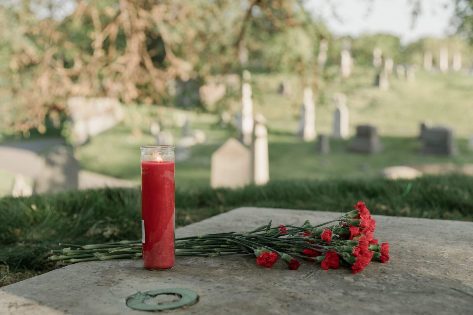 A candle and flowers on the ground in front of some graves.